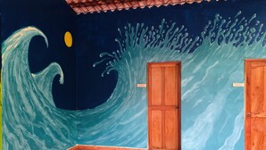 Une pièce ornée d’une fresque représentant une vague, avec une porte en bois et un sol carrelé.
