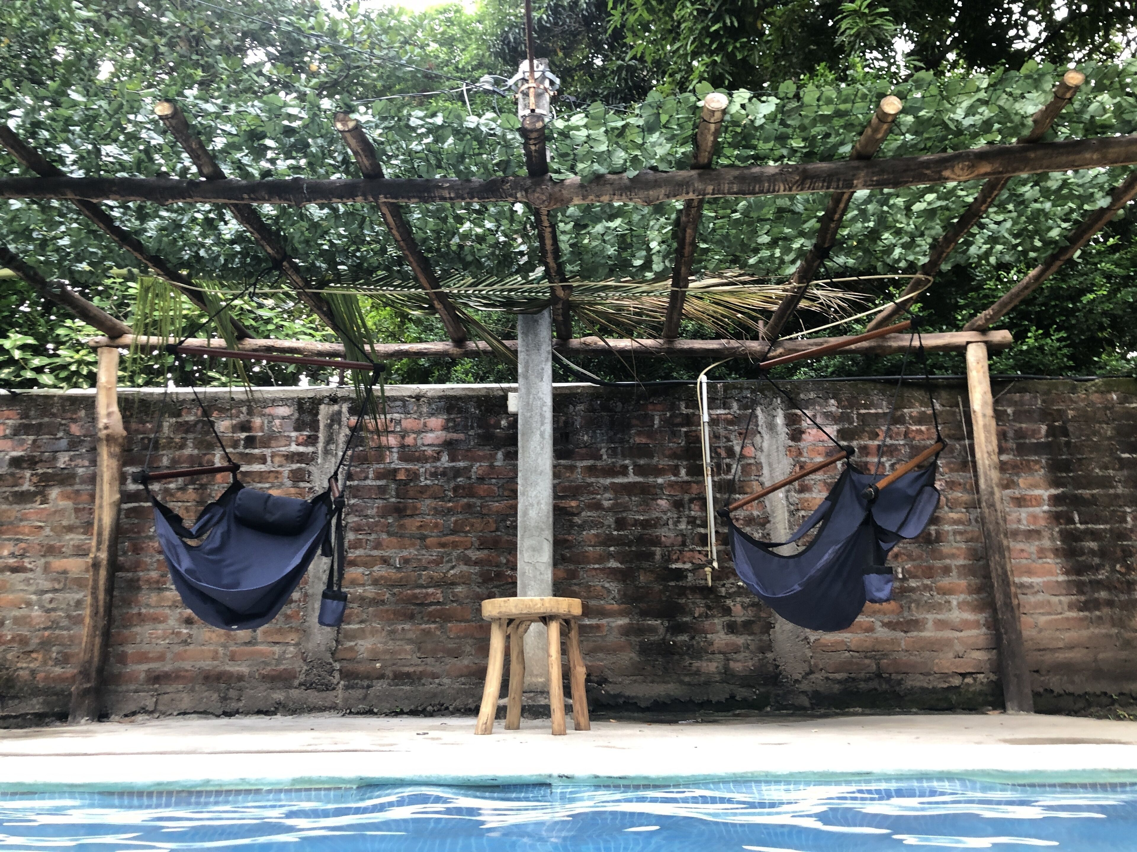 Un área de piscina con dos hamacas colgadas de una pérgola de madera.