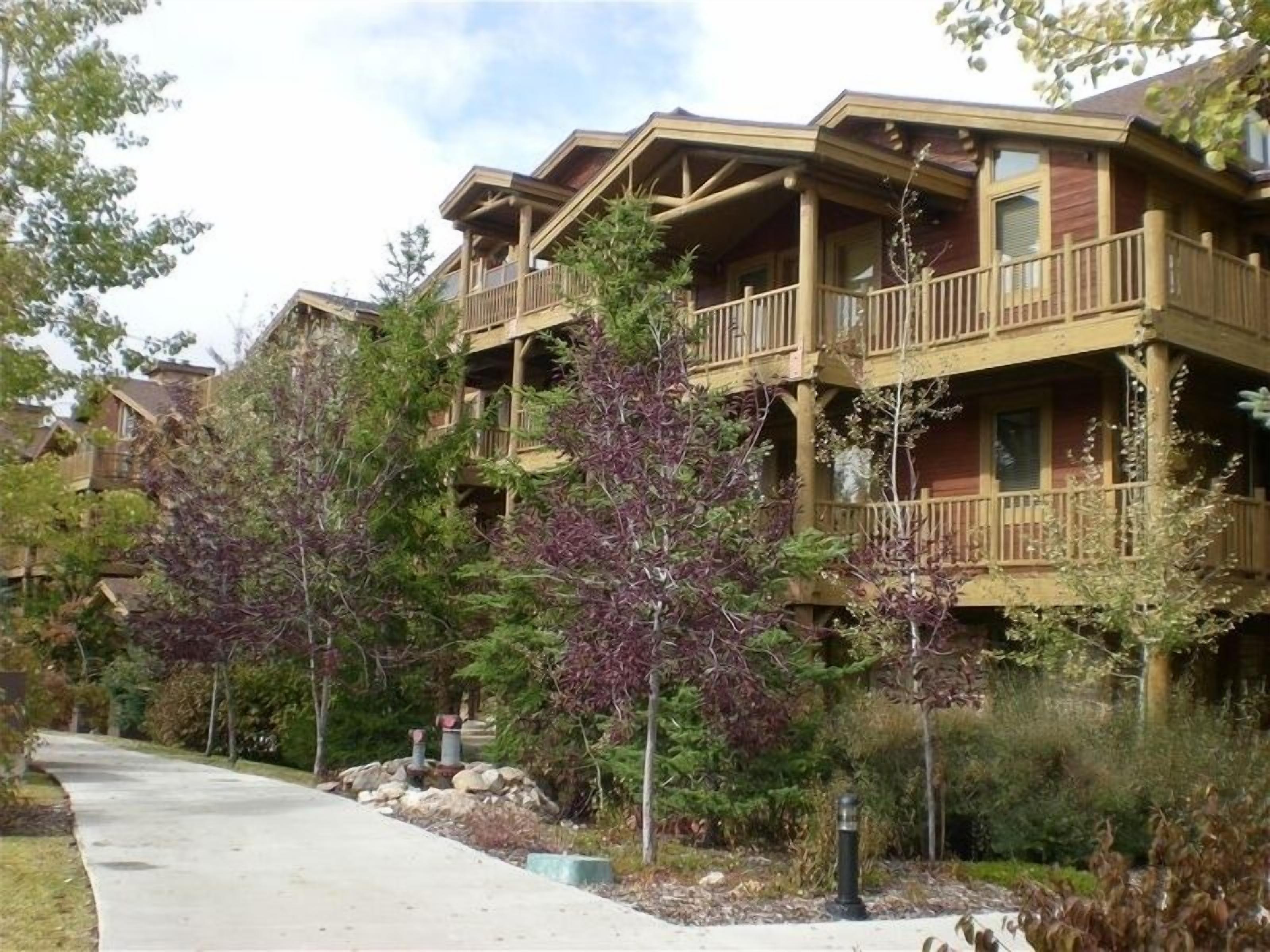 A multi-story lodge with balconies, surrounded by trees and a paved walkway.