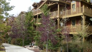 Una cabaña de varios pisos con balcones, rodeada de árboles y un sendero pavimentado.