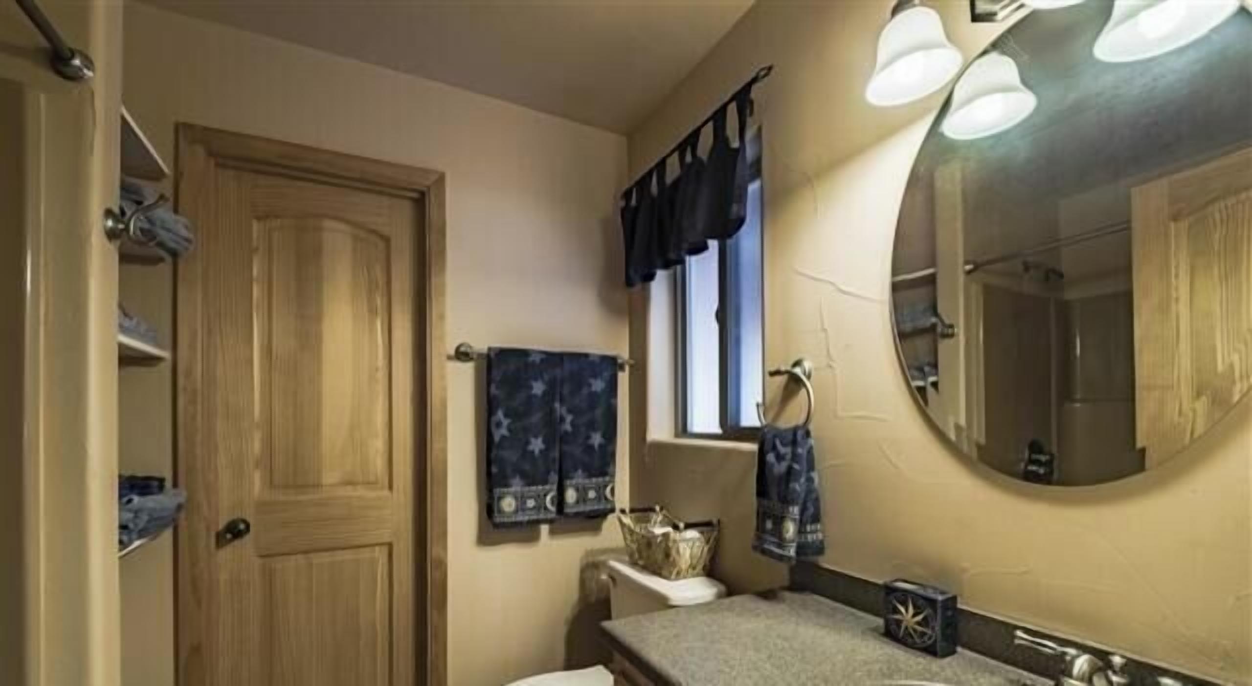 Een badkamer met een houten deur, een raam met gordijn, een spiegel en een handdoekhouder.