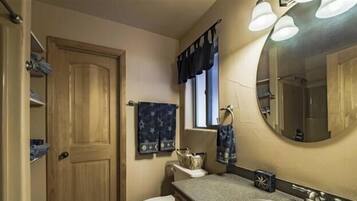Een badkamer met een houten deur, een raam met gordijn, een spiegel en een handdoekhouder.
