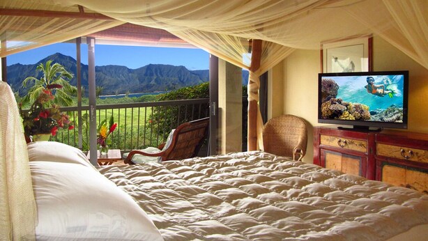 A bedroom with a bed, a television, a chair, and a view of mountains. - Hanalei Bay Resort Ocean Front Unobstructed Bali Hai View!  (princeville)