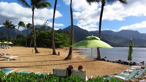 A beach with lounge chairs, umbrellas, and palm trees. - Hanalei Bay Resort Ocean Front Unobstructed Bali Hai View!  (princeville)