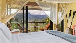 A hotel room with a bed, a small table, and a chair. There is a balcony with a view of mountains and greenery. - Hanalei Bay Resort Ocean Front Unobstructed Bali Hai View!  (princeville)