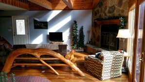 Una sala de estar acogedora con un sillón de balancín de madera, un sillón estampado, una chimenea y una pared de piedra.