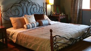 Un dormitorio con una cama grande, ventilador de techo, mesita de noche con lámpara y ventana con cortinas.