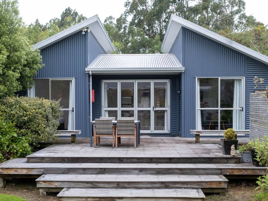 A blue house with a deck, large windows, and a door.