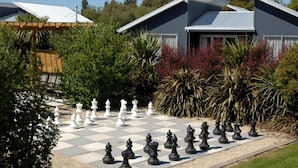 Um tabuleiro de xadrez montado em uma área do jardim, com uma casa ao fundo.