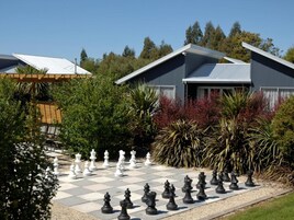 Un tablero de ajedrez dispuesto en un jardín, con una casa al fondo.