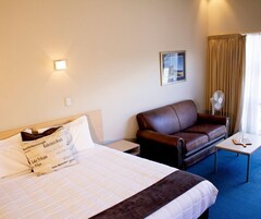 Habitación de hotel con una cama, un sofá de cuero marrón, una mesita con un vaso y un ventilador de pared.