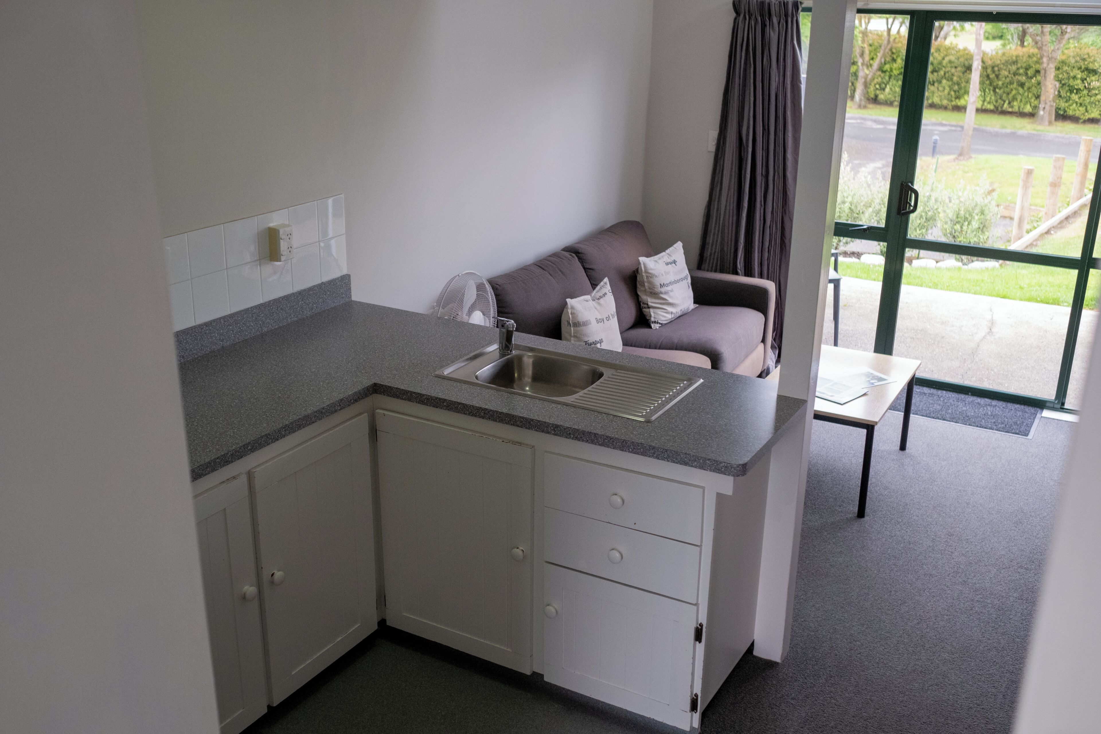 A compact kitchenette with a sink, cabinets, and a window with a view of the outdoors.