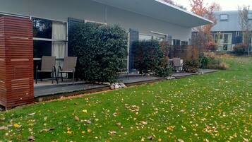 A modern house with a covered patio, a lawn with scattered leaves, and a brick wall.
