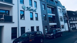 Un moderno edificio de hotel con un letrero llamativo que dice "Hotel", varias ventanas y un estacionamiento con dos coches.