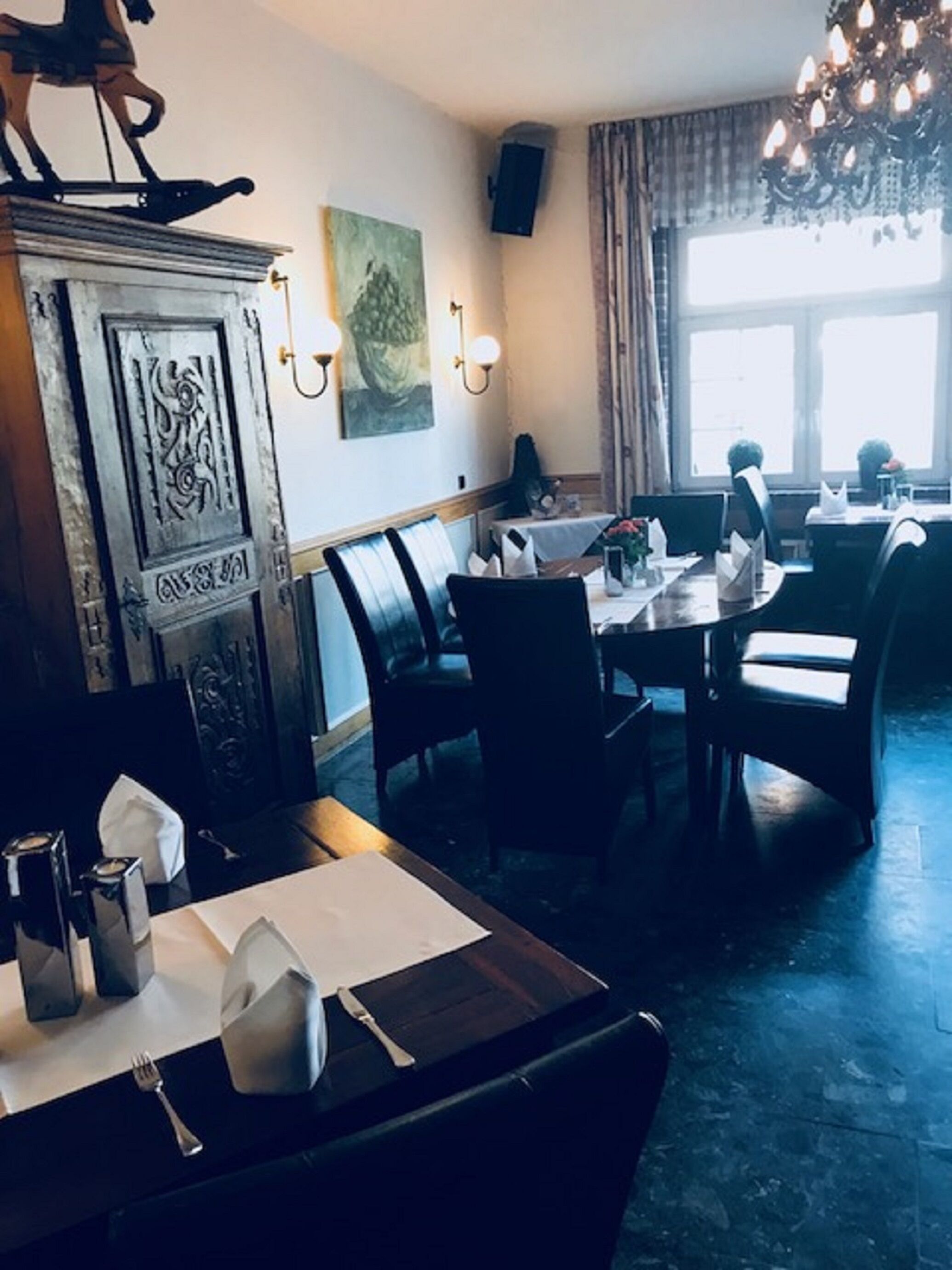 Ein Restaurantinneres mit einer Holztruhe, Esstischen, Stühlen und einer Kandelaber.