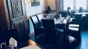 Ein Restaurantinneres mit einer Holztruhe, Esstischen, Stühlen und einer Kandelaber.