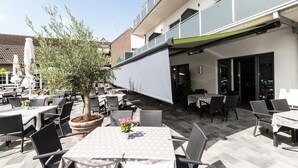 Un patio al aire libre con mesas y sillas, una planta en maceta y un edificio con balcón.