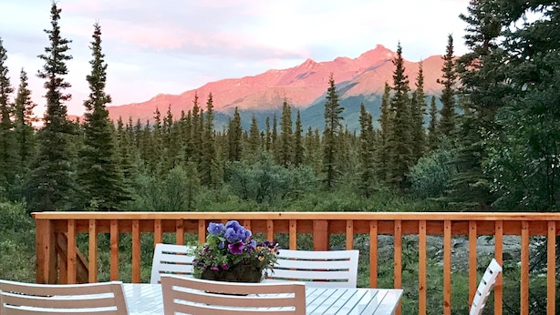 Una terraza de madera con una mesa, sillas, una maceta y vistas a la montaña.