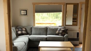 Una habitación acogedora con un sofá seccional gris, una mesa de madera y una cama con manta blanca.