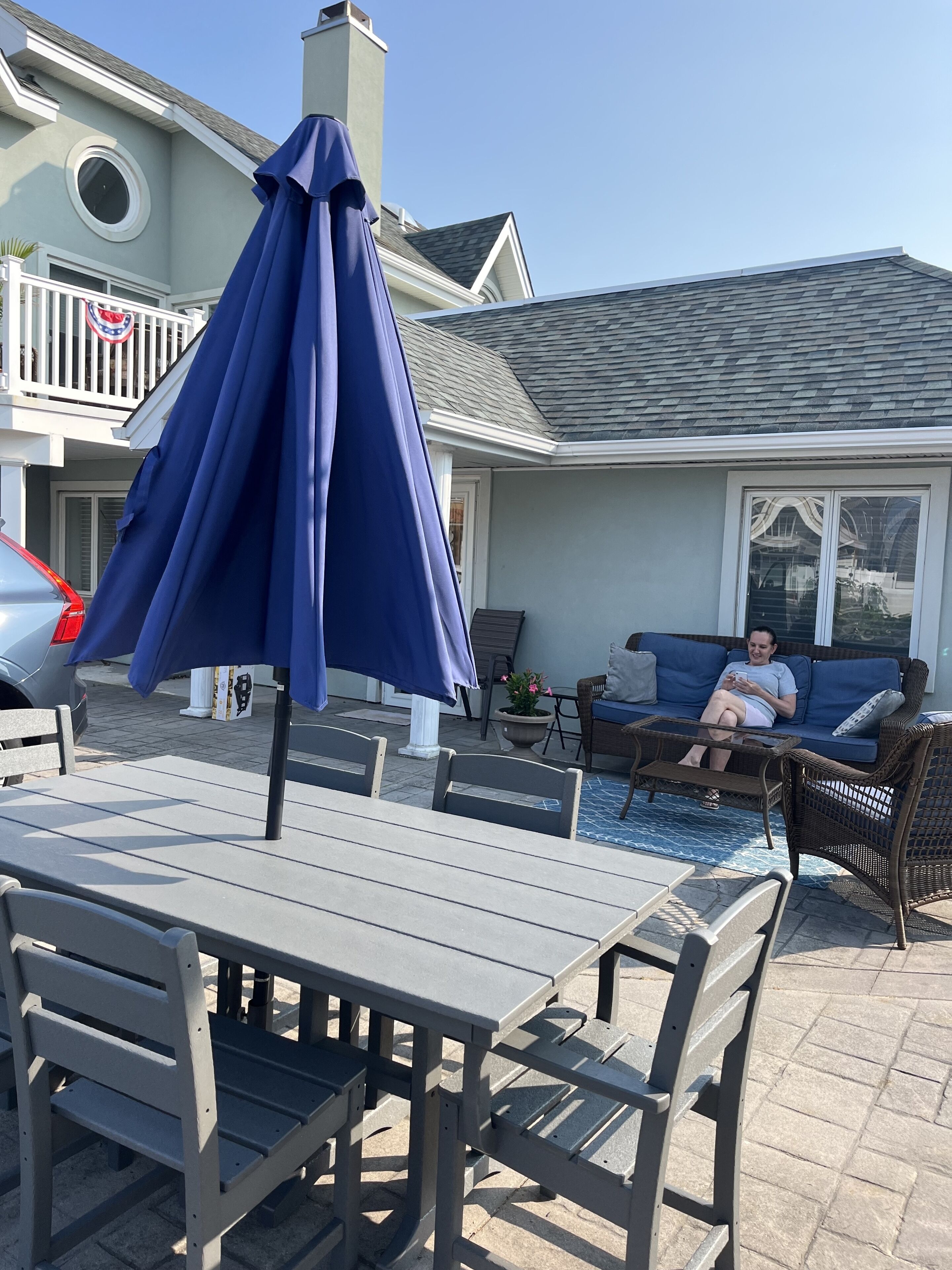 An outdoor patio with a table and chairs, a blue umbrella, and a person sitting on a couch.