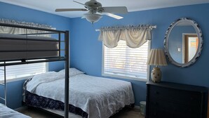 Un dormitorio con literas, ventilador de techo, ventana con persianas, cómoda y espejo.