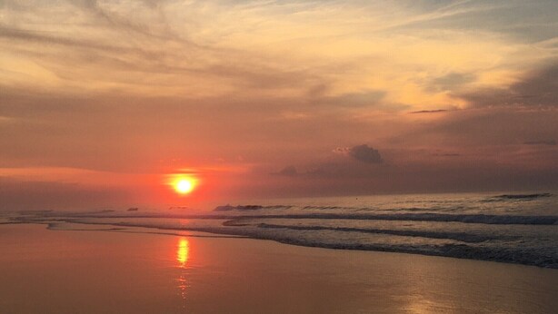 Un atardecer sobre una playa con olas y un cielo despejado.