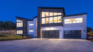 Une maison moderne à deux étages, dotée d’un grand garage, de grandes fenêtres et d’une allée bien éclairée.