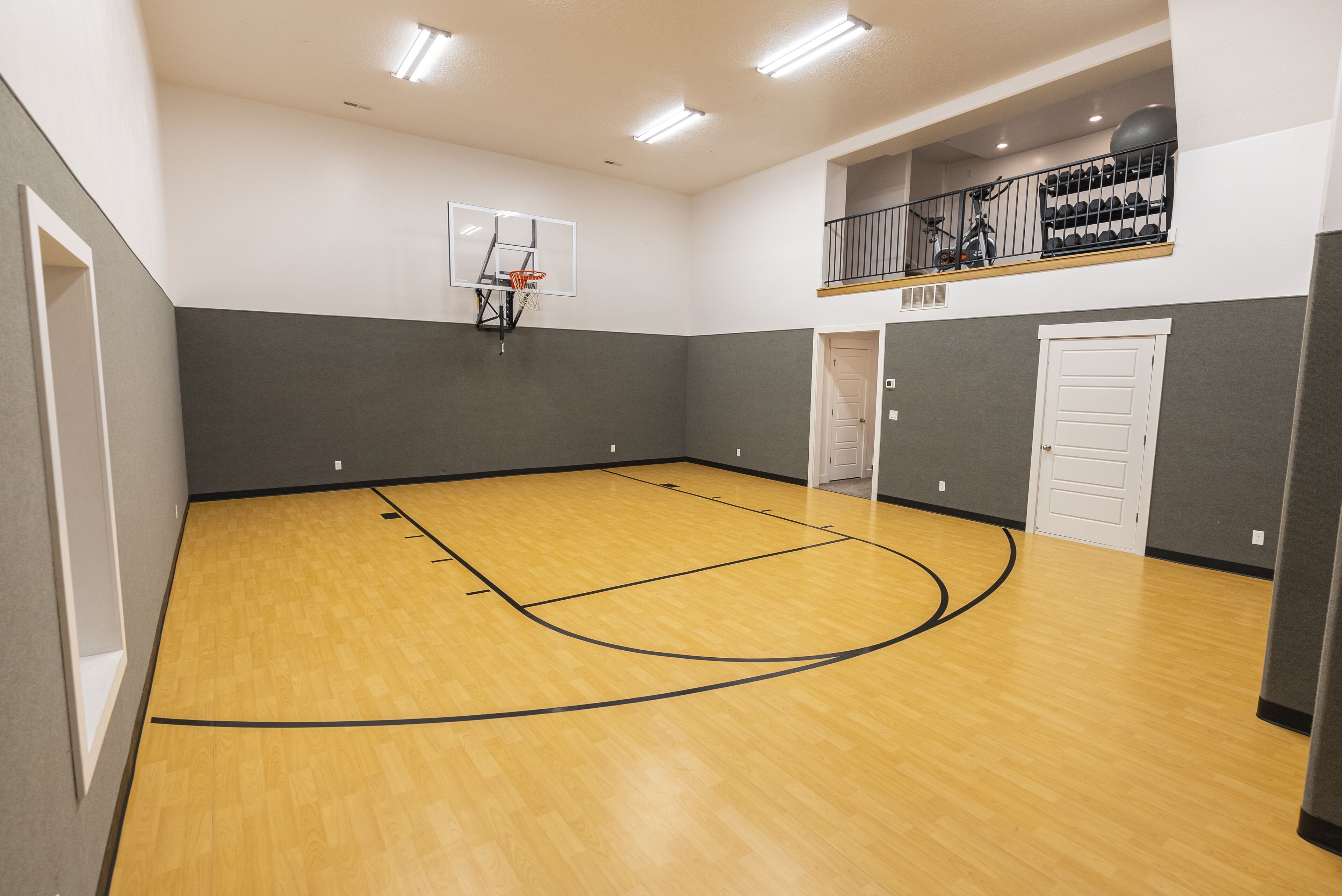 Ein Basketballplatz mit Basketballkorb, einer Tür und einer Treppe, die zu einem Balkon mit Fitnessgeräten führt.