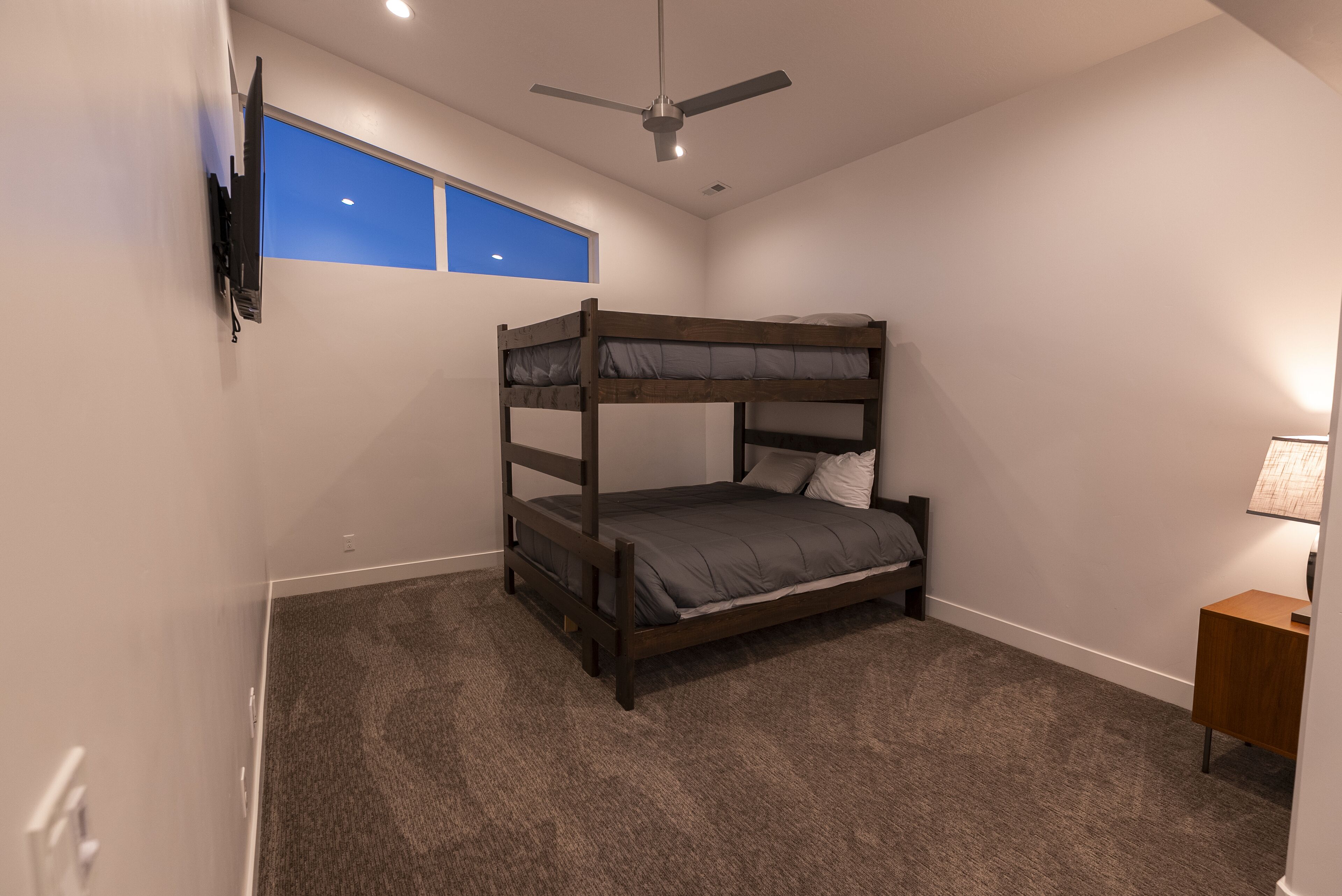 Habitación con literas, ventilador de techo, televisor montado en la pared y ventana con vistas.