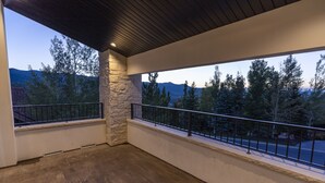 Un balcon doté de piliers en pierre, d’un plancher en bois et offrant une vue sur les arbres et les montagnes.
