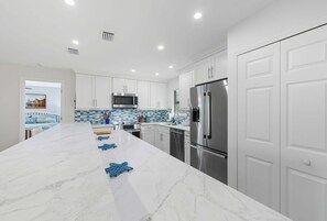 A modern kitchen with white cabinetry, a large marble island, stainless steel appliances, and a checkered backsplash.