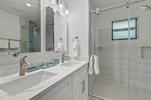 Une salle de bain moderne dotée d’un grand miroir, de deux lavabos et d’une douche à parois de verre.