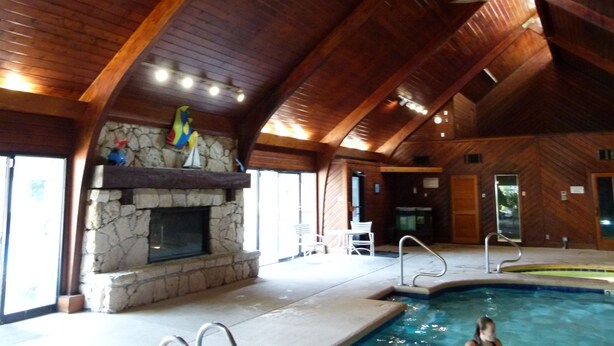Amplia zona de piscina interior con chimenea de piedra, vigas de madera en el techo y pared de piedra.