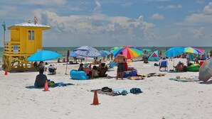 Una playa con una torre de salvavidas, sombrillas y gente.
