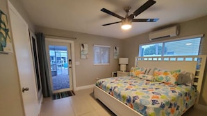 Ein Schlafzimmer mit Bett, Deckenventilator, Fenster und einer Tür, die auf einen Balkon führt.