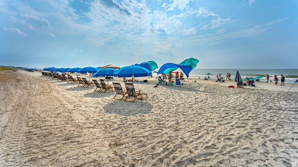 A beach with rows of blue umbrellas and beach chairs, a sandy shore, and the ocean in the background. - 117 Heated Pool | Elevator | Kids Retreat | Sleeps Big Families | Pet Friendly (Hilton Head Island)