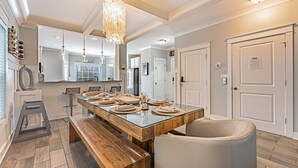 A modern kitchen with a long wooden table set for dining, a bench, and a hanging light fixture. - 117 Heated Pool | Elevator | Kids Retreat | Sleeps Big Families | Pet Friendly (Hilton Head Island)