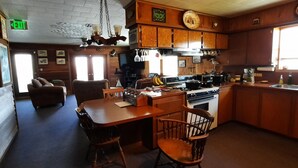 Un restaurante acogedor con decoración de madera, un comedor con sillas, una cocina con estufa y ollas, y un ventanal con luz natural.
