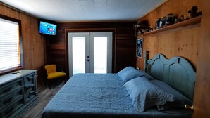 Un dormitorio con cama, una silla, televisión y puerta.