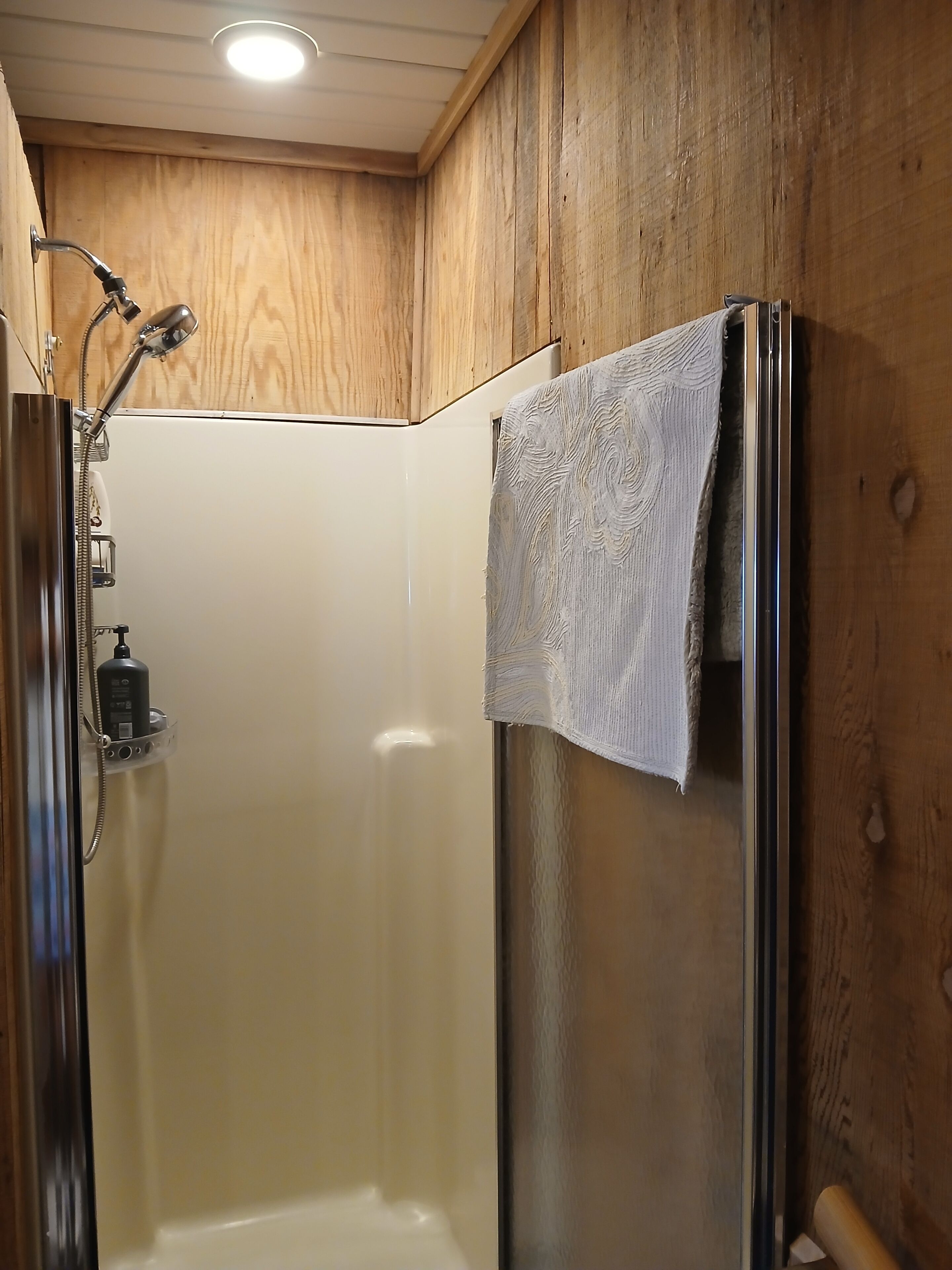 Een douche met een handdouche, een glazen deur en een handdoek aan de muur.
