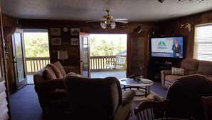 Una sala de estar acogedora con televisor, asientos cómodos y un balcón con terraza de madera.