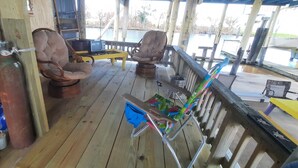 Una terraza de madera con dos sillas de mimbre, una mesita y una silla plegable azul.