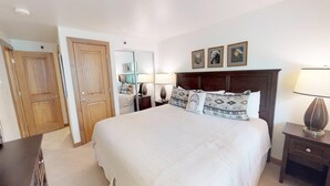 A bedroom with a large bed, wooden doors, a nightstand, and a lamp. - Terracehouse - Steps to Slopes - Hot Tub/Pool - ASE Transportation (Snowmass Village)