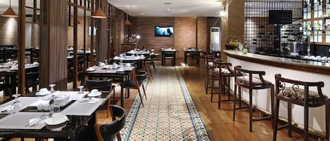 A restaurant with a long dining area, a bar, and a TV screen on the wall.