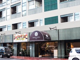 Entrada de hotel com placa indicando Manila Lotus Hotel, sinal de estacionamento e um pinheiro de Natal lá fora.