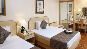 A DELUXE ROOM with two beds, a bedside table with a lamp, a phone, and a framed picture on the wall.