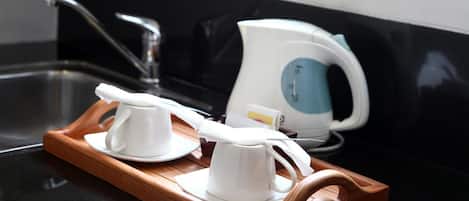 Una encimera de cocina con una bandeja de madera que sostiene dos tazas blancas y una tetera eléctrica blanca.