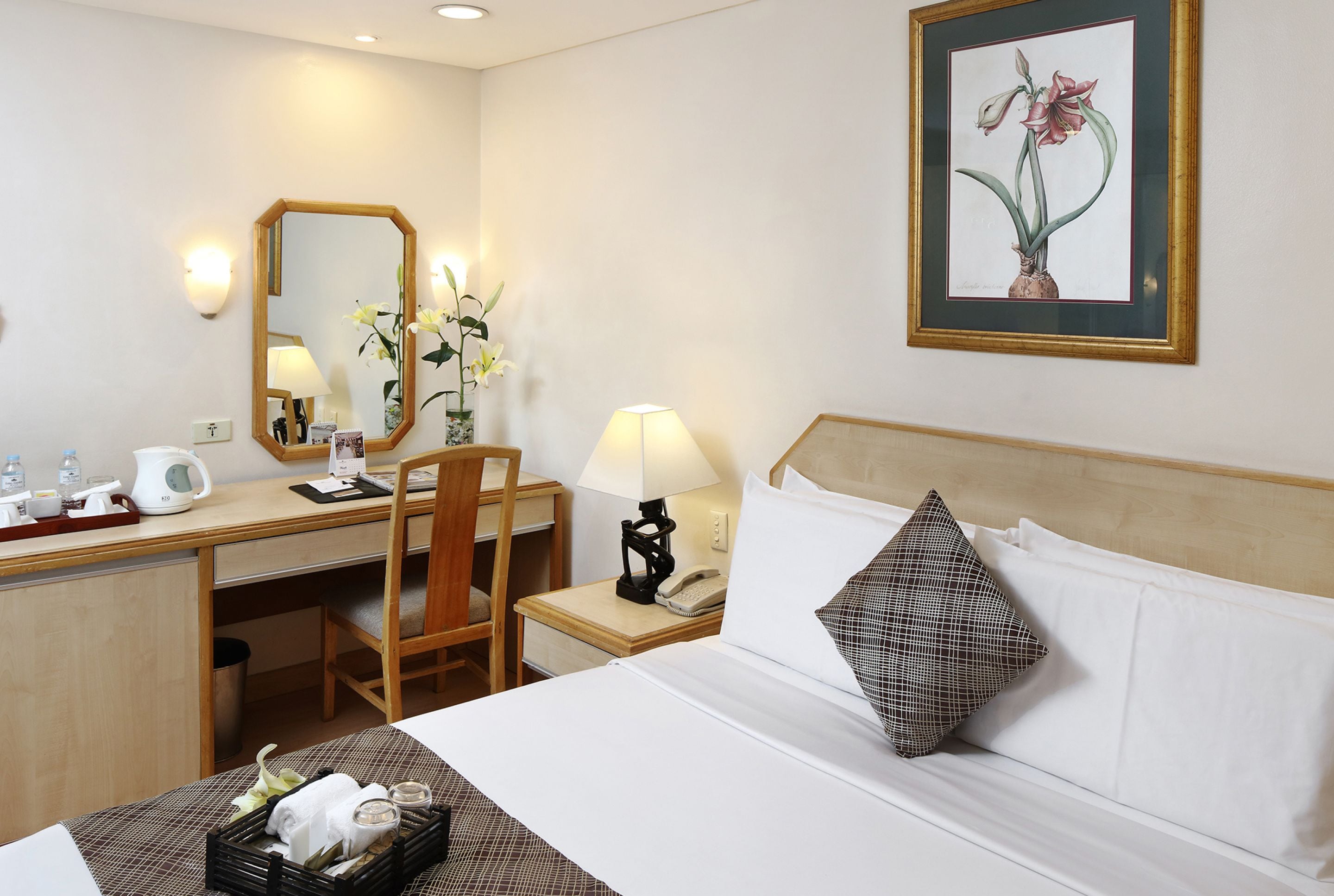 Una habitación de hotel con una cama, un escritorio, una silla, una lámpara, un teléfono, un espejo y un cuadro en la pared.