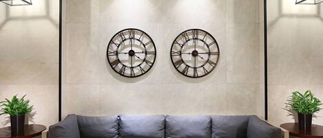 Una sala de estar moderna con un sofá gris, dos relojes de pared y dos mesitas de noche con plantas en macetas.