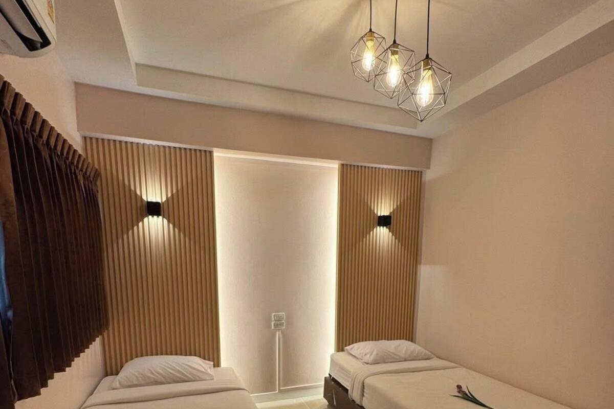 A hotel room with two beds, a modern ceiling light fixture, and a large window with blinds.